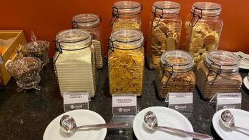 Een ontbijtbuffet met diverse cornflakes en granola opties in glazen potten, elk voorzien van het merk 'Nord'.