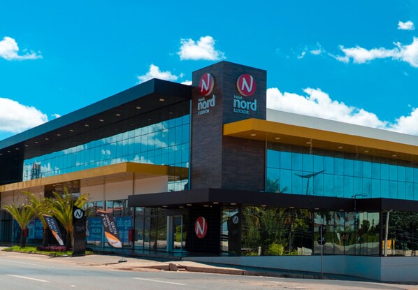 A modern hotel with a glass facade, prominent signage, and a clear blue sky. - Nord Luxxor Juazeiro (Juazeiro do Norte)
