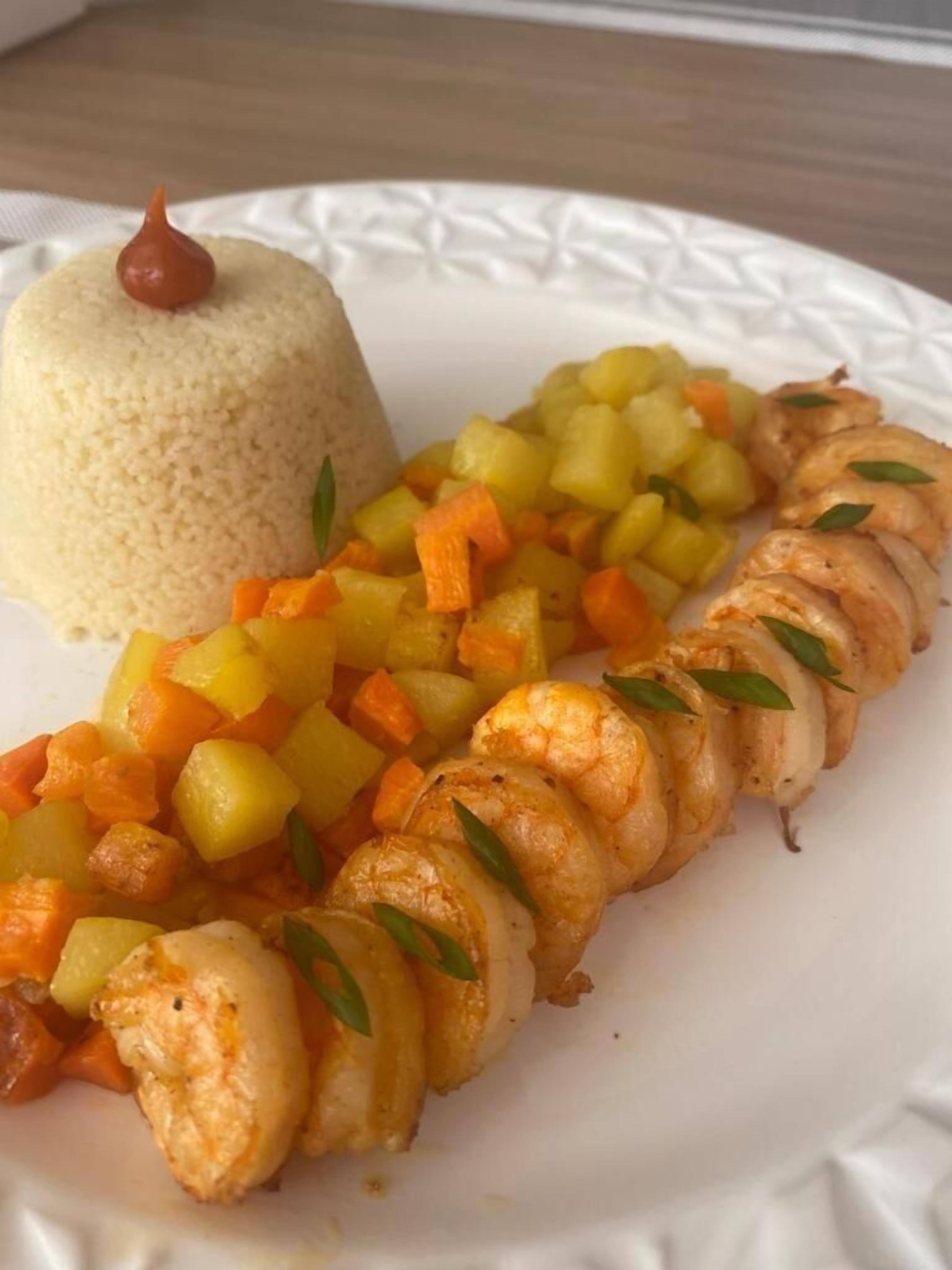 A plate with a mound of couscous, a side of diced vegetables, and a spiral of shrimp.