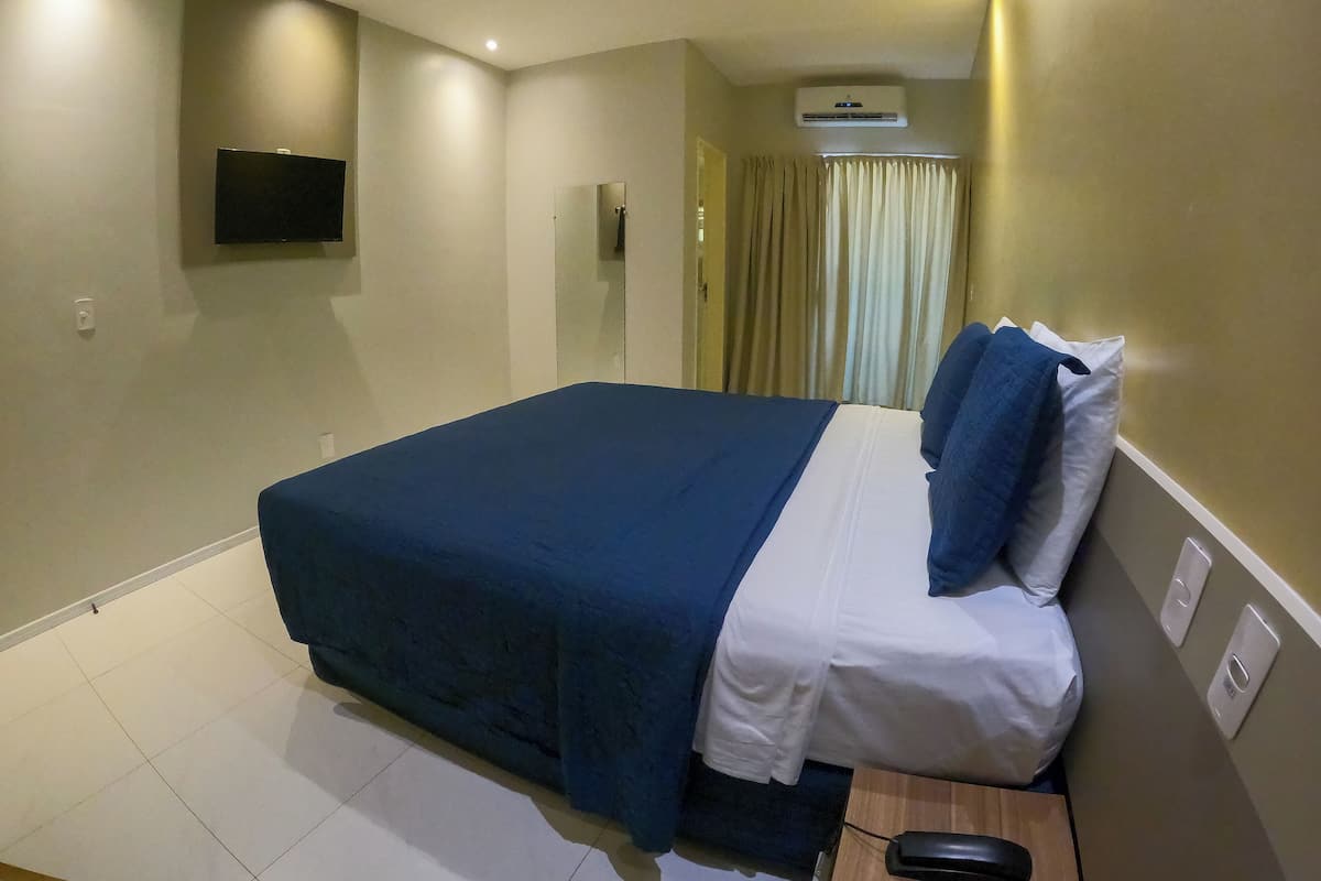 A hotel room with a bed, a flat-screen TV mounted on the wall, and a window with curtains.