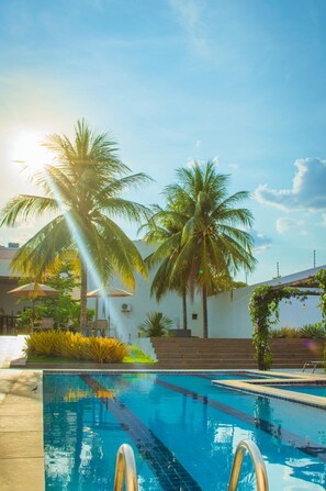 Una piscina con agua azul cristalina, rodeada de palmeras y un edificio blanco.