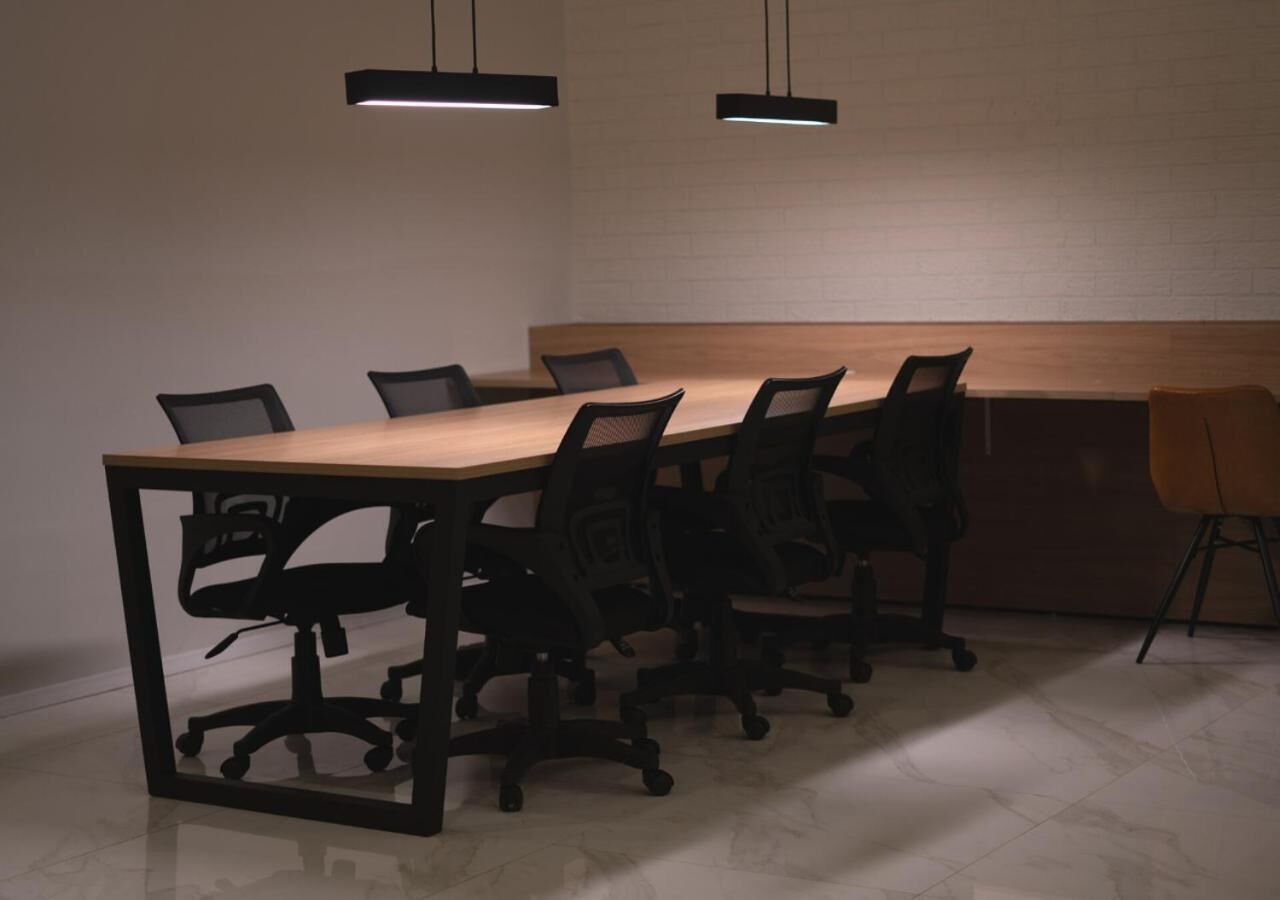 A conference room with a long table, black office chairs, and pendant lighting.