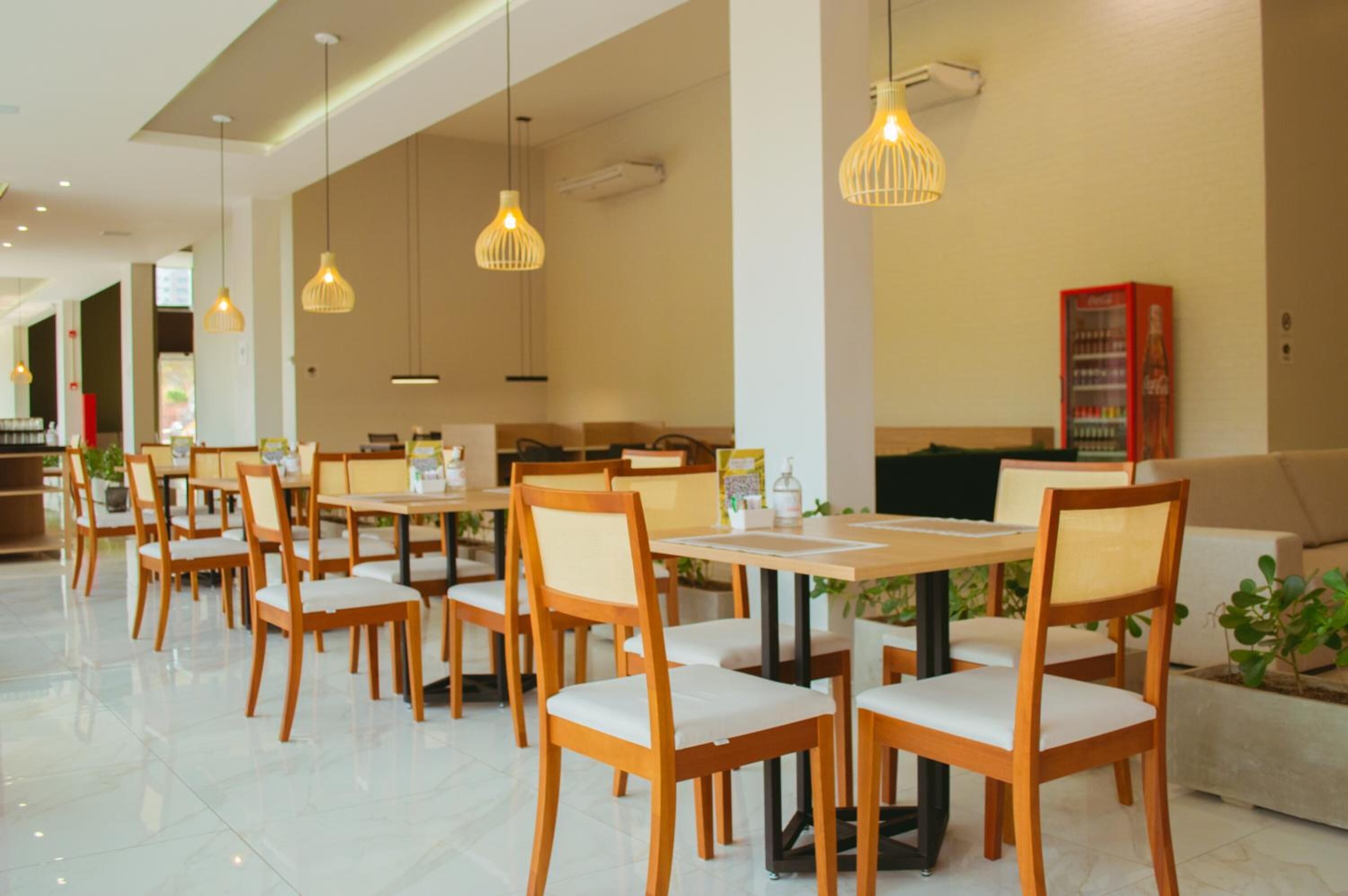 A spacious dining area with wooden tables and chairs, pendant lighting, and a vending machine.