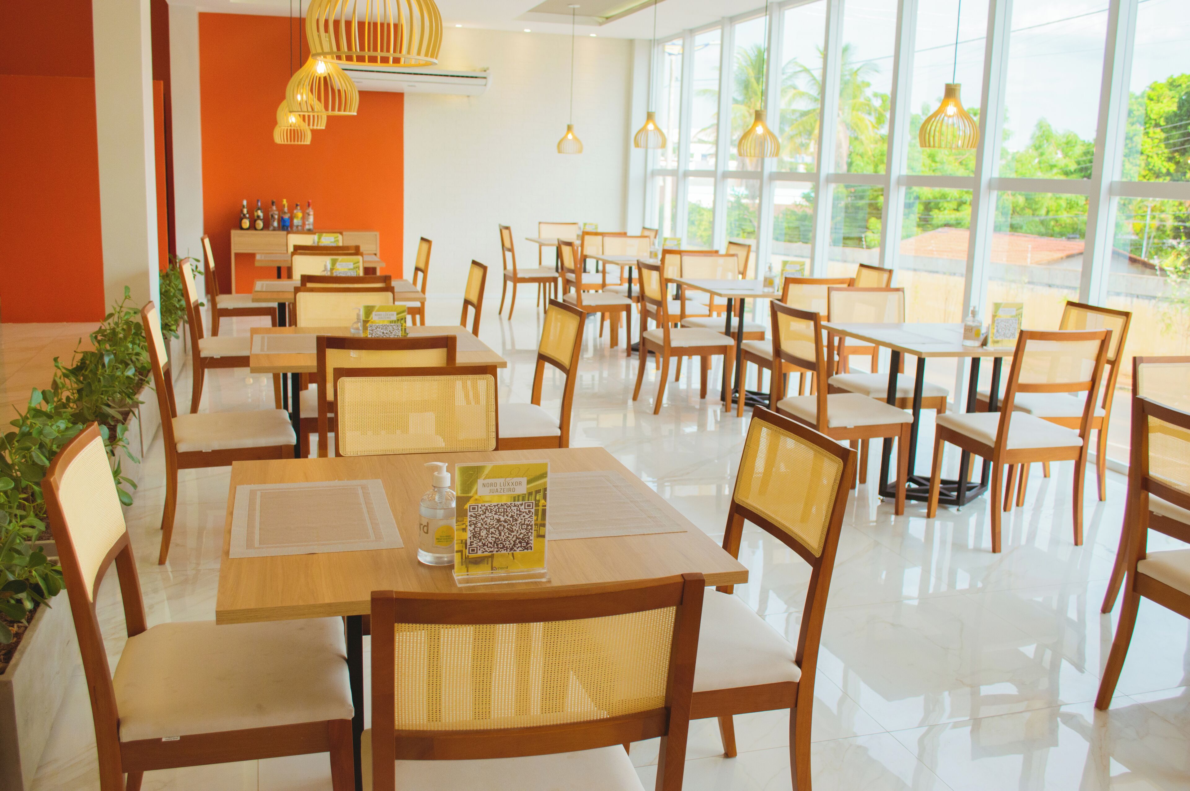 A spacious dining area with multiple tables and chairs, large windows offering a view of greenery outside, and a clean, modern interior design.