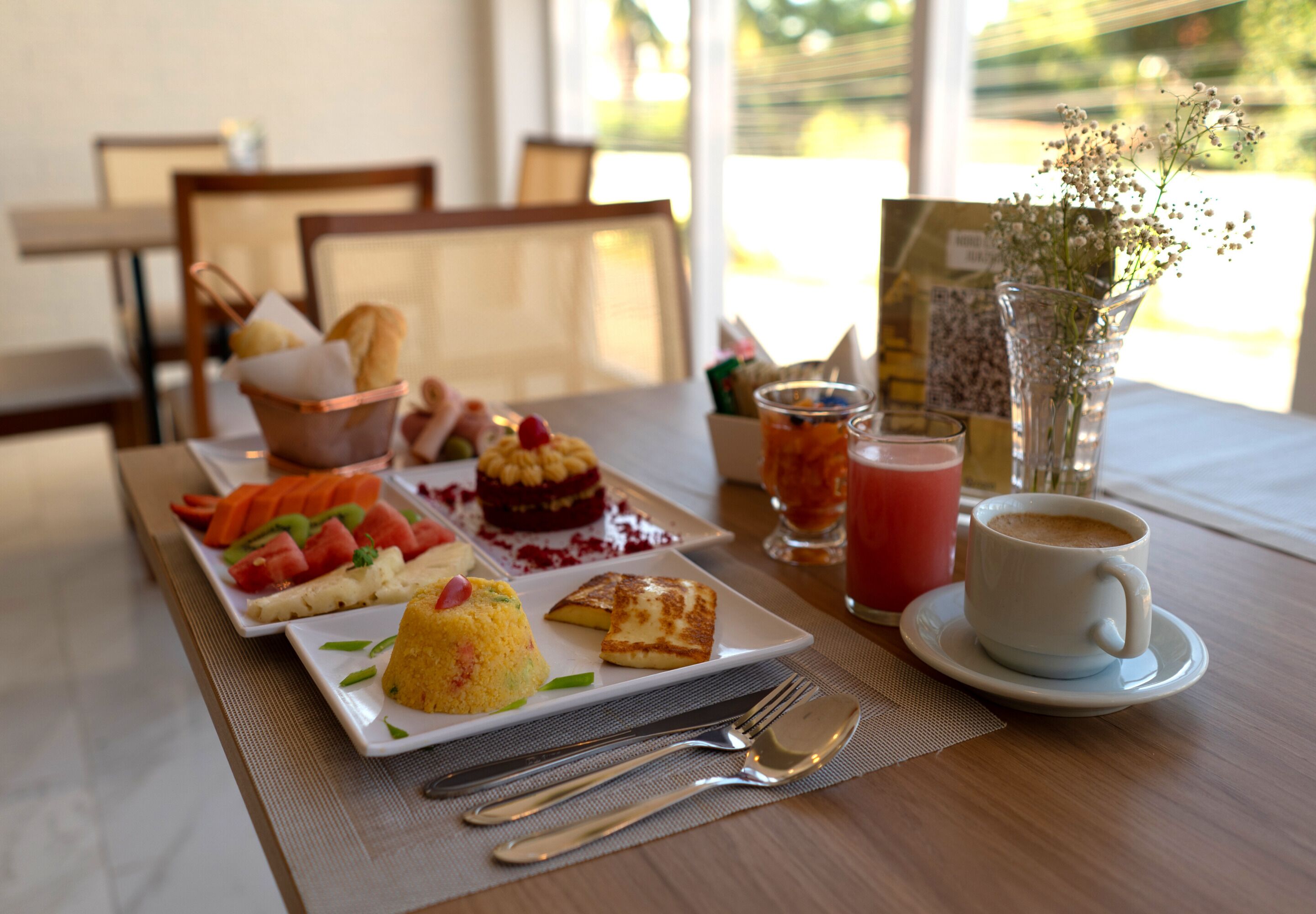 A breakfast setting with a variety of dishes, including pancakes, a fruit salad, and a dessert, along with coffee and juice.