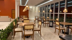 Un comedor moderno con mesas y sillas de madera, iluminación colgante y ventanas amplias.