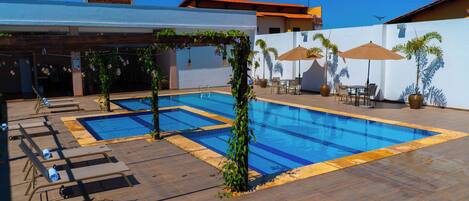 A swimming pool area with lounge chairs and umbrellas.
