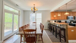 A spacious kitchen with wooden cabinets, a large island, and a dining area with a long table and chairs. - Amazing Central Location! Lakefront! Hot tub/dock! (Oakland)