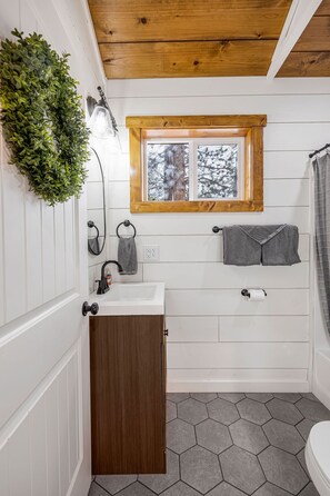 A bathroom with a wooden ceiling, a window with a view of trees, a sink with a towel, and a toilet. - SUPER CUTE & CLEAN MODERN HOME 40 min. to YNP (Island Park)