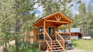 A wooden cabin with a porch, a small deck, and a hanging flower basket. - SUPER CUTE & CLEAN MODERN HOME 40 min. to YNP (Island Park)