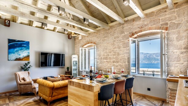 Un salon chaleureux avec une table basse en bois, des sièges confortables, un téléviseur et un mur en pierre agrémenté d’une fenêtre offrant une vue pittoresque.