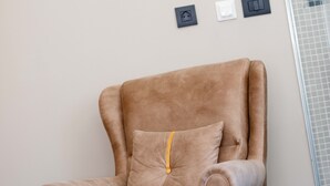Un fauteuil marron avec un coussin, placé contre un mur où se trouvent trois prises électriques.