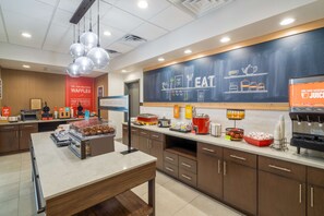 A modern cafe with a chalkboard menu, a coffee machine, and a variety of food items displayed on the counter. - Hampton Inn Hardeeville (Hardeeville)