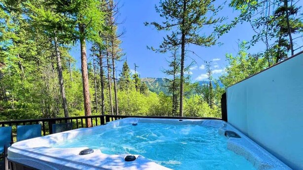 A hot tub set on a deck with a forest backdrop. - Ski Access | Hot Tub | 2 King Beds | Fireplace (Whitefish)
