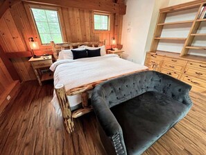 Un dormitorio tipo cabaña de madera con cama, mesitas de noche, una silla y un aparador de madera.