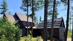 A cabin with a sloped roof, surrounded by tall trees and dense underbrush. - Ski Access | Hot Tub | 2 King Beds | Fireplace (Whitefish)