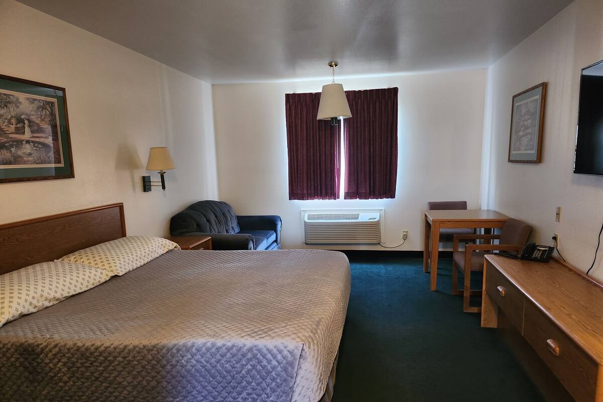A hotel room with a bed, a desk, a chair, a lamp, a TV, and a window with curtains.