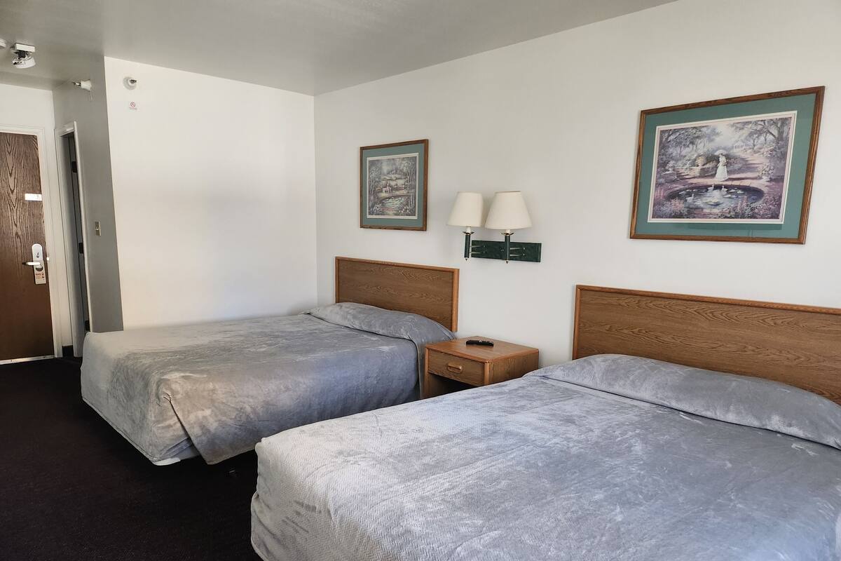 A hotel room with two beds, a nightstand with lamps, and two framed pictures on the wall.