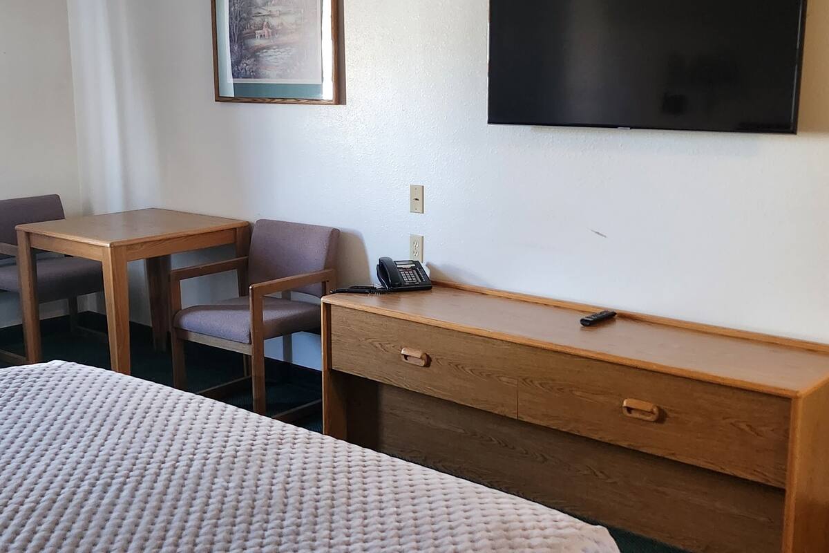 A hotel room with a bed, a desk, a chair, a television, and a painting on the wall.