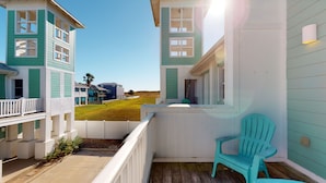 A coastal property with a balcony featuring a turquoise chair, a white railing, and a view of the beach and neighboring houses. - Shared Pool and Hot Tub, Golf Cart Access (Port Aransas)
