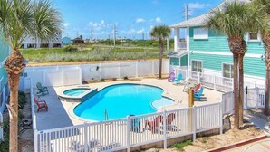 A swimming pool with a white fence, palm trees, and a blue house in the background. - Shared Pool and Hot Tub, Golf Cart Access (Port Aransas)