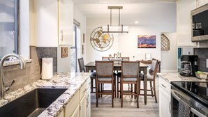 A modern kitchen with granite countertops, a central island, and a dining area with wooden chairs.