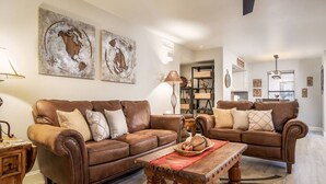 A living room with two brown leather sofas, a wooden coffee table, and a bookshelf.