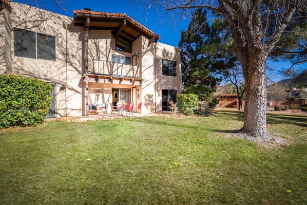 A two-story house with a patio area, a tree in the front yard, and a clear blue sky.