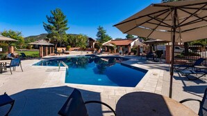 A swimming pool with lounge chairs and umbrellas, surrounded by buildings and trees.