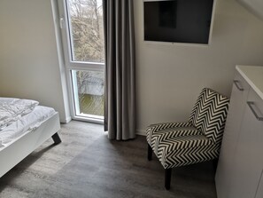Une chambre à coucher avec un lit, une chaise, une télévision et une fenêtre avec des rideaux.