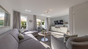 Een moderne woonkamer met een bank, fauteuil, salontafel en een televisie.