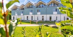 A modern multi-story residential building with balconies, a paved driveway, and a grassy area.