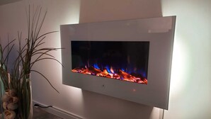 Un téléviseur à écran plat fixé au mur, sur lequel est affichée une image de cheminée avec des flammes.