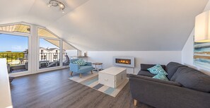 A spacious loft-style living area with a fireplace, large windows, and a view of the outdoors.