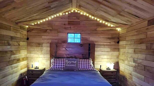 Une chambre confortable dans un chalet en bois, avec un lit, des tables de chevet et des guirlandes lumineuses.