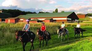 Un groupe de personnes à cheval dans un champ verdoyant, avec des granges en arrière-plan.