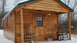 Une cabane en bois avec un toit vert, une porte d’entrée et deux fauteuils à bascule à l’extérieur.