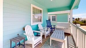 Eine überdachte Veranda mit weißen und blauen Adirondack-Stühlen, einem kleinen Tisch und einem weißen Geländer.