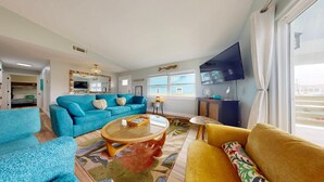 Un salon avec un canapé bleu, un canapé jaune, une table basse ronde et un téléviseur à écran plat fixé au mur.