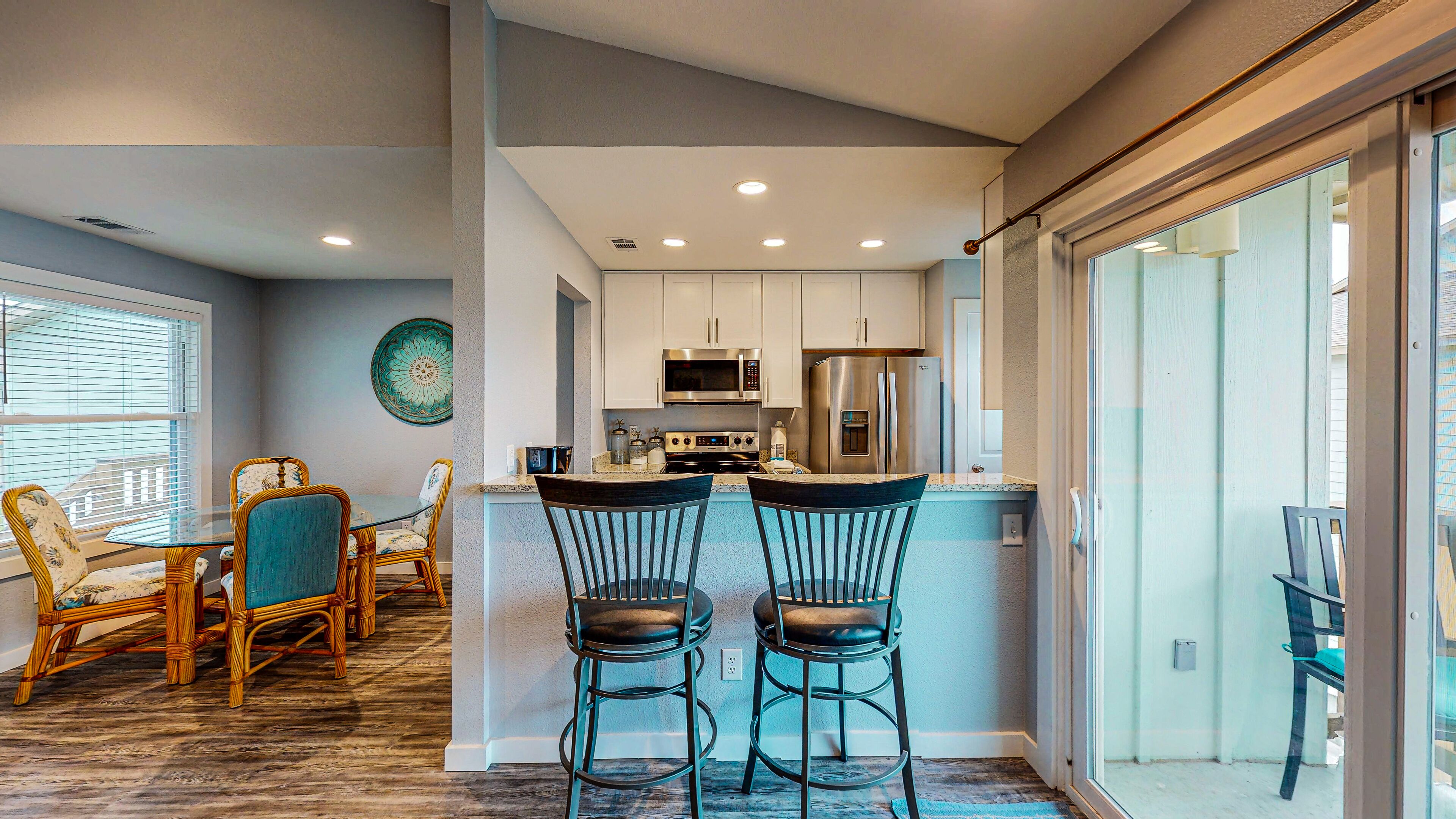 A modern kitchen with white cabinets, stainless steel appliances, and a dining area with wicker chairs and a glass table.