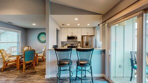 A modern kitchen with white cabinets, stainless steel appliances, and a dining area with wicker chairs and a glass table. - 2nd Floor, Shared Pool, Pet Friendly, Golf Cart Access (Port Aransas)