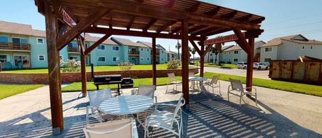 A covered outdoor patio with tables and chairs, a barbecue grill, and a sign indicating a requirement for a parking permit.