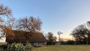 A rural property with a large open grassy field, a windmill, and a building with a dark roof. - Bluebonnet Ridge -- Historical Family Farm! (Belton)