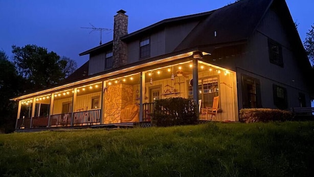 A two-story house with a stone chimney, a covered porch with string lights, and a well-maintained lawn. - Bluebonnet Ridge -- Historical Family Farm! (Belton)