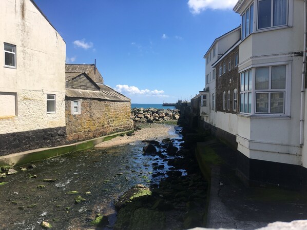 A narrow waterway between buildings with a rocky shore and a pier in the distance.