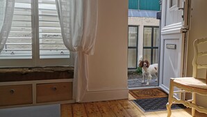A room with a wooden floor, a white chair, a window with white curtains, and a door leading outside.