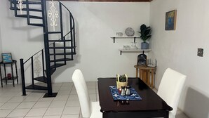 Ein Essbereich mit einem schwarzen Tisch, weißen Stühlen, einer schwarzen Wendeltreppe und Regalen mit Dekorationen.