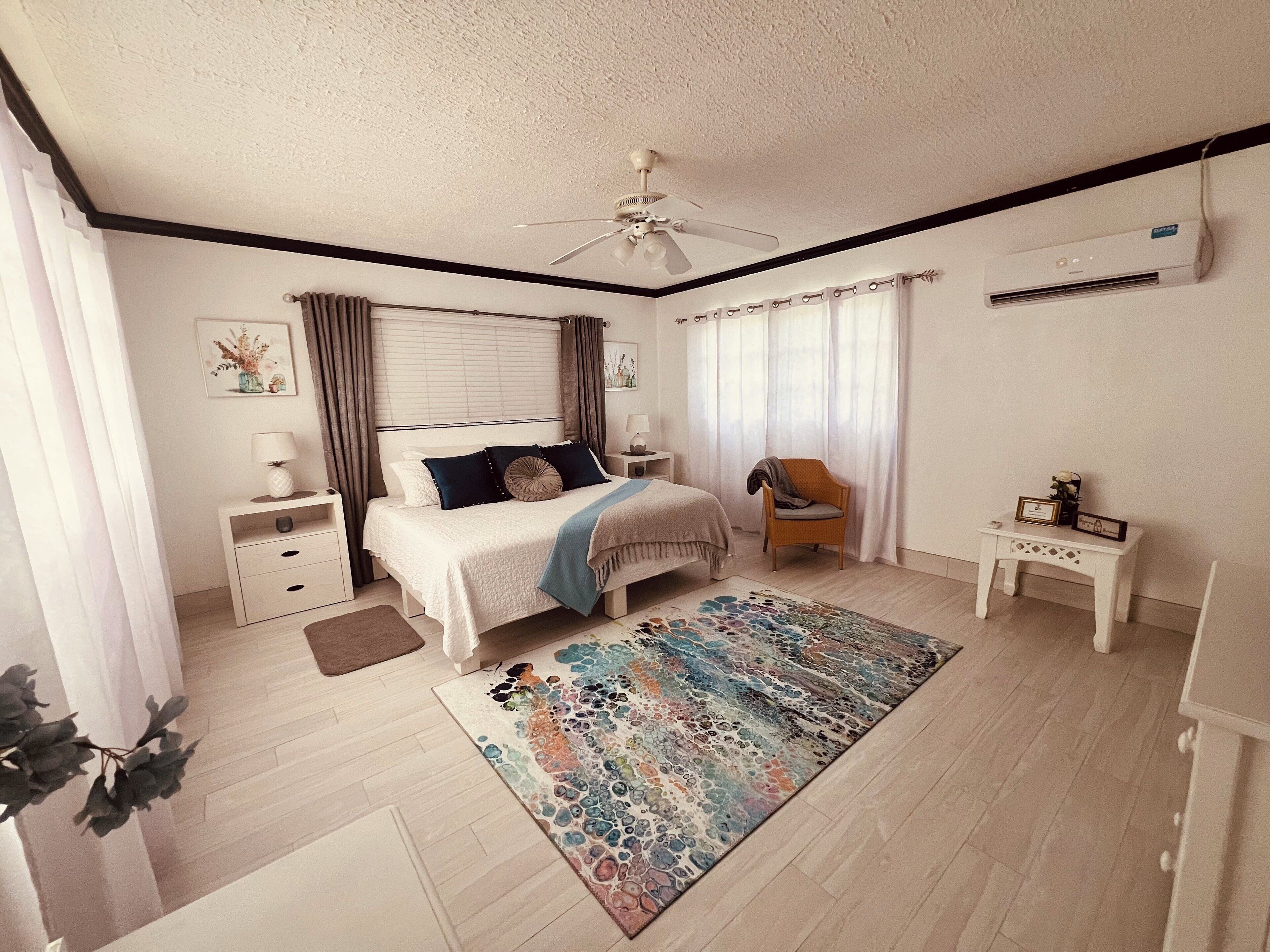 Une chambre à coucher comprenant un lit, des tables de chevet, une chaise, un bureau, un ventilateur de plafond et un climatiseur.