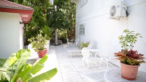 Eine Terrasse mit weißer Gartenmöbeln, Topfpflanzen und einem Gebäude mit Kachelböden.