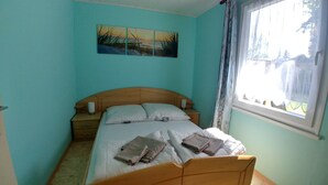 Un dormitorio con cama, mesita de noche, lámpara y ventana con cortinas.